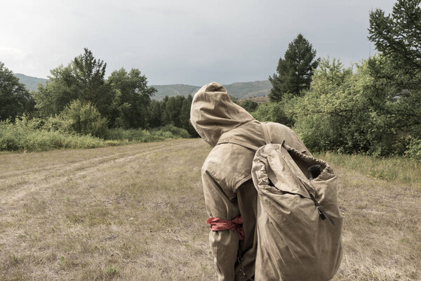 Back view of tourist man with a backpack standing ready to travel on green forest background. Stalker in the post-apocalyptic world.