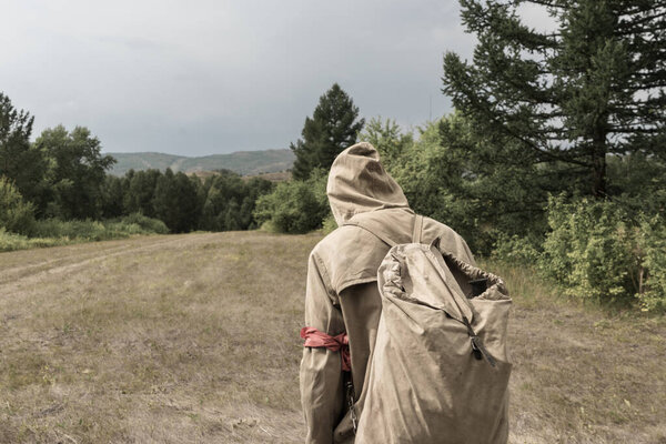 Back view of tourist man with a backpack standing ready to travel on green forest background. Stalker in the post-apocalyptic world.