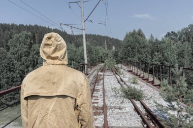 Adam terk edilmiş bir demiryolu köprüsünde duruyor. Yolun karşısındaki ormanda eski bir demir köprü.