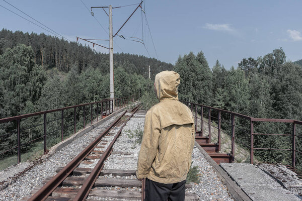 man stands on an abandoned railway bridge. old iron bridge in the forest across the road