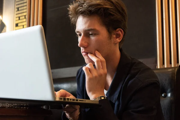 young man sits at a table in front of a laptop. man working at laptop