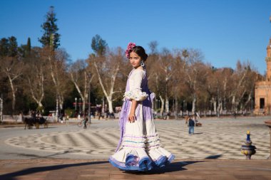 İspanya 'da, Seville' de ünlü bir meydanda bej renkli bir elbise ve fırfırlı mor bir elbise içinde flamenko dansı yapan küçük bir kız. Kızın kafasında çiçekler var ve saçı topuz gibi.