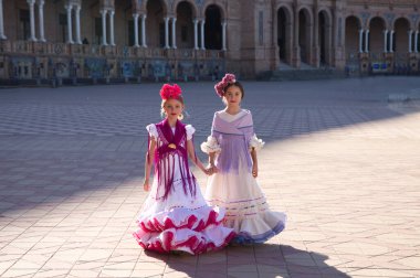 Tipik çingene kostümleriyle flamenko yapan iki güzel kız Sevilla 'da ünlü bir meydanda el ele yürüyorlar. Kızlar çok mutlu. Flamenko, insanlığın kültürel mirası.
