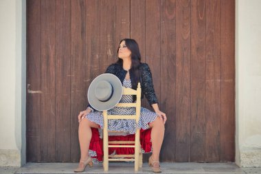 Latin kadın, genç ve güzel, dans eden flamenko, eski bir tahta sandalyede oturuyor. Kadın, siyah benekli, kısa siyah ceketli, beyaz bir elbise giyiyor.