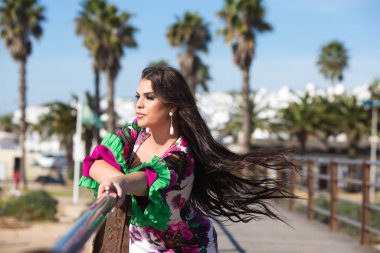 Latin bir kadın, genç ve güzel dans eden flamenko saçları havada elini ve kolunu korkuluklara uzatıyor. Dalgalı ve çiçekli beyaz elbiseli kadın tipik Endülüs.