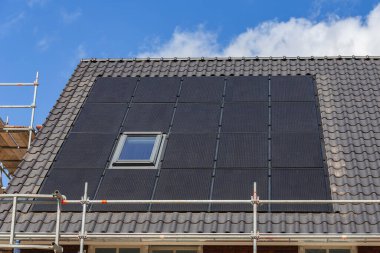 Mavi gökyüzüne karşı yeni binaların kiremitli çatılarındaki güneş panelleri.