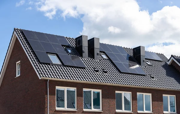 Mavi gökyüzüne karşı yeni binaların kiremitli çatılarındaki güneş panelleri.