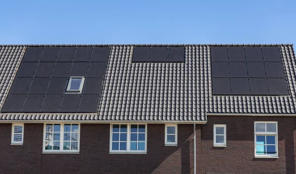 Mavi gökyüzüne karşı yeni binaların kiremitli çatılarındaki güneş panelleri.