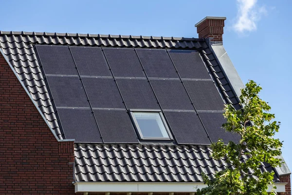 Mavi gökyüzüne karşı yeni binaların kiremitli çatılarındaki güneş panelleri.