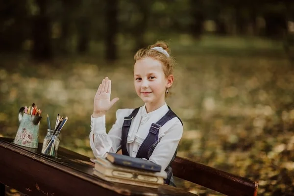 Portrait of young funny school girl sitting on a wooden desk. Hand up. Back to school. Copy space