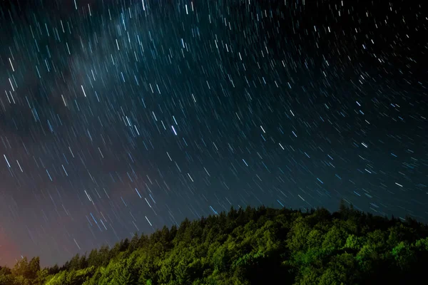 Gece boyunca hareket eden yıldızların manzarası, ormanın yakınında.
