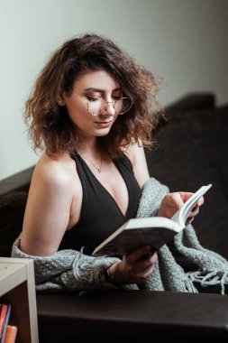 Kanepede kitap okuyan güzel bir kız resmi..