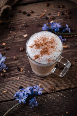 Ahşap arka planda mavi çiçekli latte macchiato bardağı.