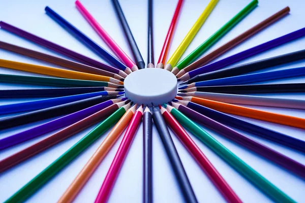 Resmin ortasında bulunan yuvarlak beyaz bir silginin etrafına bir dizi renkli kalem serilmiştir. Beyaz bir arka planda gün ışığında çekilmiş.