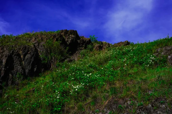 The landscape is black rocks, a blue sky with floating clouds and a lot of green grass and white flowers. Spring. Summer. Heat. Nature is beautiful. Fresh air