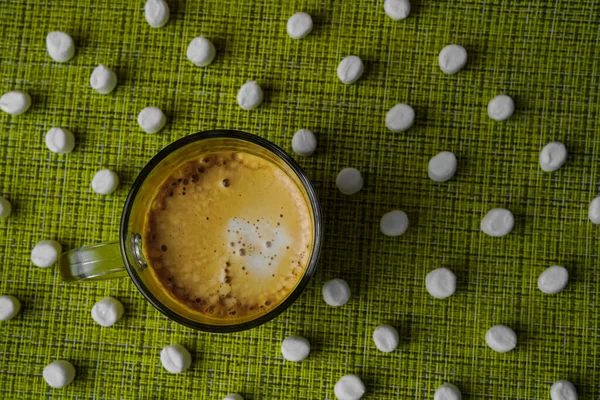 Birçok beyaz marşmelov yeşil ve sarı bir hasır peçeteye dizilmiştir. Alışılmadık bir tatlı fotoğrafı. Tatlı olarak lezzetli yemekler. Kremalı kahve fincanı.