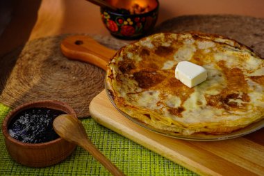 Yuvarlak krepler ve bir dilim tereyağı tahta kesme tahtasının üzerinde duruyor. Yakınlarda böğürtlen reçelli yuvarlak bir bambu tabağı var. Tüm aile için lezzetli bir kahvaltı.