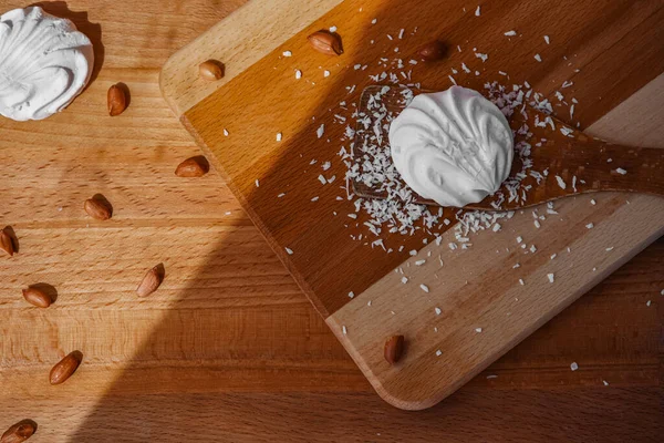 Marshmallow pişiriyorum. Tahta bir masa ve kürek üzerinde, bitmiş bir tatlı, ceviz ve hindistan cevizi etrafında. Pişirme malzemeleri. Beyaz atıştırmalıklar. Fotoğraf yukarıdan çekildi.