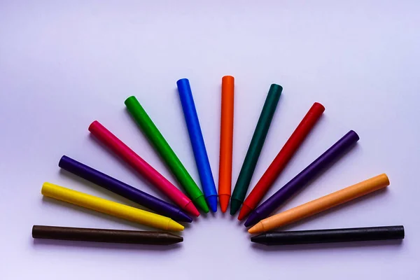 Beyaz arka planda yarım daire şeklinde 12 renkli mum boya kalemi serili.