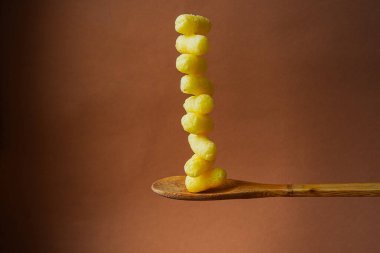 Sarı mısır çubukları büyük bir tahta kaşıkta istiflenir. Kahverengi arka plan. Soyut resim. Sıra dışı yemek fotoğrafı..