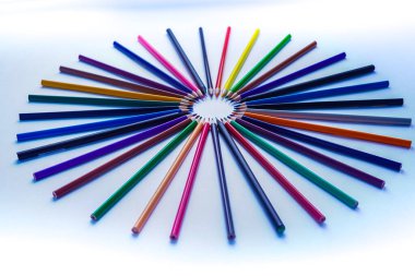 Birçok renkli kalem seti fotoğrafın merkezinde bir daire şeklinde dizilmiştir. Çerçeve gün ışığında beyaz bir arkaplanda çekilmiş.