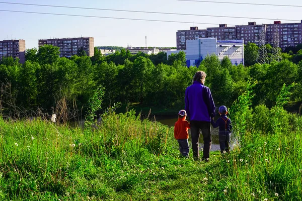 Aile - baba ve iki çocuk sırtüstü duruyor, şehir binalarının mesafesine bakıyorlar. Doğa - yeşillik, ağaçlar. Güneşli gün batımı.