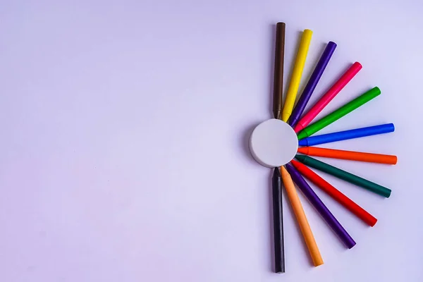 12 renkli mum boya kalemi beyaz arkaplandaki silginin etrafında bir yarım daire şeklinde dizilmiş, yazı için yeri olan.