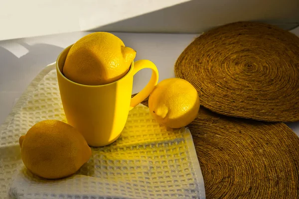 Parlak sarı limonlar ve pencere eşiğinde doğal ışıkta duran bir kupa. Gün, güneş ve gölge. Meyveler, peçeteler, fincanlar, zombisiz arka planda paraşüt altlıkları. Bahar, yaz, ılık.