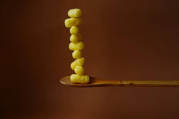 Sarı mısır çubukları büyük bir tahta kaşıkta istiflenir. Kahverengi arka plan. Soyut resim. Sıra dışı yemek fotoğrafı..