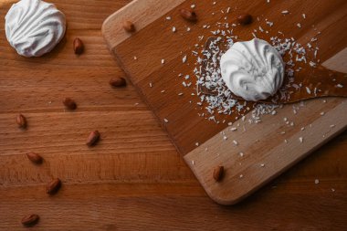 Marshmallow pişiriyorum. Tahta bir masa ve kürek üzerinde, bitmiş bir tatlı, ceviz ve hindistan cevizi etrafında. Pişirme malzemeleri. Beyaz atıştırmalıklar. Fotoğrafın perspektifi yukarıdan..