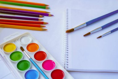 Çizim üzerinde çalışmak için bir yer. Suluboya resimler, albüm, fırçalar, renkli kalemler. Beyaz ışık arka planı. Çizim eğitimi. Yaratıcılık için sanat malzemeleri.