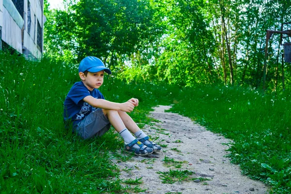 Şehir parkında, bir çocuk yeşil çimlerin üzerinde oturur. Rüya gören bir çocuk. Çocuk patikanın yakınında dinleniyor. Sağlık için temiz havada doğa yürüyüşü. Yaz, bahar, sıcak hava