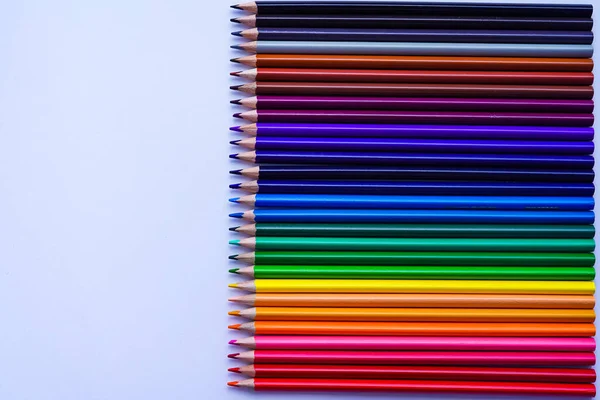 Renkli kalemlerinden bir set arka arkaya gri bir defterin üzerine serildi. Fotoğraf gün ışığında beyaz bir arkaplanda çekildi. Sol kopyalama alanı