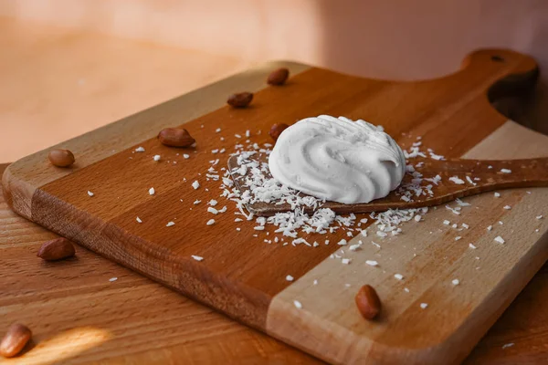 Marshmallow pişiriyorum. Tahta bir masa ve kürek üzerinde, bitmiş bir tatlı, ceviz ve hindistan cevizi etrafında. Pişirme malzemeleri. Beyaz atıştırmalıklar. Fotoğrafın perspektifi yukarıdan..