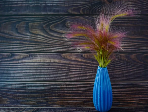 Küçük, sevimli bir buket pofuduk çivi, arka plandaki küçük mavi bir vazoda duruyor. Koyu doğal ahşap tahtalar. Resmin metin yazmak için bir yeri var. Boşluğu kopyala