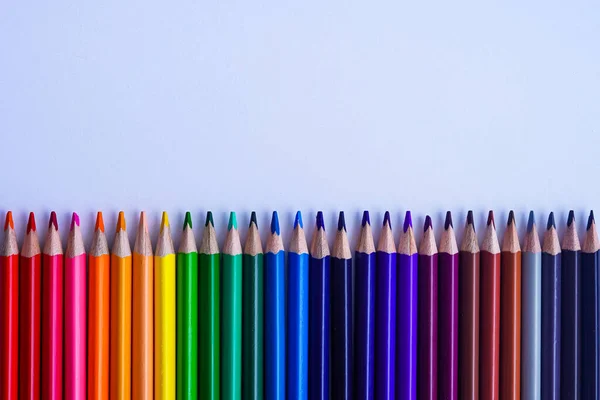 Renkli kalemlerinden bir set arka arkaya gri bir defterin üzerine serildi. Fotoğraf, gün ışığında beyaz bir arkaplanda çekildi. Üst kopyalama alanı.