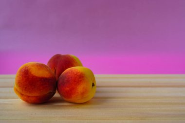 Üç sulu olgun şeftali, parlak pembe arka plandaki doğal ahşap ışık panolarının üzerinde yatıyor. Taze meyve - sağlık ve düzgün beslenme için vitamin ve tatlı kaynağı, diyet