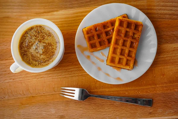 Taze Viyana waffleları yuvarlak bir tabakta ve çatalda yatıyor. Sıcak aromatik kahve. Tahta kahverengi masa. Tatlı tatlı. Öğle yemeği için yemek. Fırın ürünleri. Yemek pişirmek. Bir restorandan ya da ev yapımı tabaklar