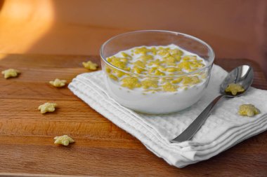 Sağlıklı ve lezzetli bir kahvaltı. Yıldızlar şeklinde mısır gevreği. Tahta bir masanın üzerindeki beyaz pamuk peçetenin üzerindeki cam kasede süt. Sağlıklı beslenme - sağlıklı yaşam