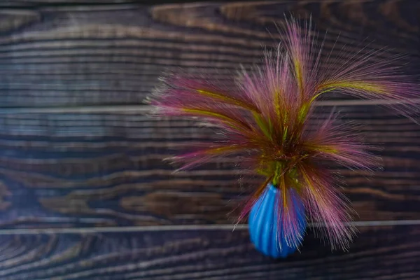 Görüntü yüksek bir açıdan çekiliyor. Düz bir çiçek buketi, koyu doğal ahşap tahtalardan oluşan küçük mavi bir vazoda duruyordu. Resmin metin yazmak için bir yeri var. Boşluğu kopyala