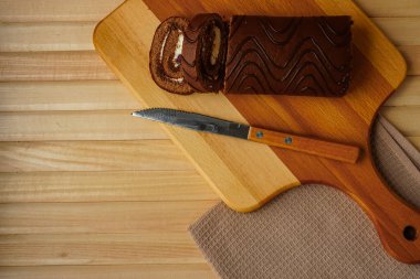 Doğal ahşap tahtalardan yapılmış hafif bir masada bir pamuk peçete ve üzerinde bir bıçağın bulunduğu bir tahta kesme tahtası var. Yuvarlak ve ev yapımı taze hamur işleri şeklinde lezzetli bir çikolatalı kek.