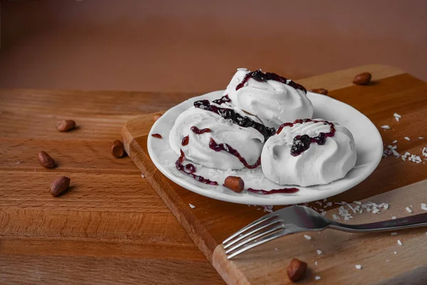 Tahta bir masanın üzerinde beyaz yuvarlak bir tabak ve üç şekerleme var. Tatlıya hindistan cevizi serpiştirilir ve reçelle sulanır. Etrafı fındık dolu. Zarif metal çatal.