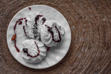 Doğal kordondan yapılmış bir peçetenin üzerinde beyaz yuvarlak bir tabak ve üç şekerleme var. Tatlıya hindistan cevizi serpiştirilir ve reçelle sulanır. Fotoğraf yukarıdan çekildi.