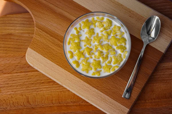 Düzgün beslenme, kahvaltıda taze sütle yıldız şeklinde mısır gevreği. Cam kase. Yakınlarda metal bir kaşık var. Tahta dokuma masası. Güzel yemek fotoğrafı.