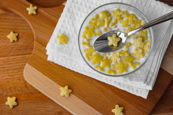 Sütlü gevrekler beyaz bir peçetede cam bir tabakta, tahta kesme tahtası, ahşap desenli bir masa. Kaşık ve yiyecek. Sağlık, diyet ve kilo kaybı için kullanışlı besin.