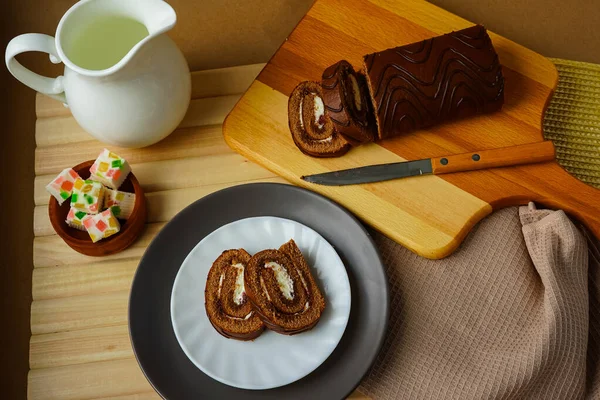 Fotoğraf yukarıdan çekildi. Tatlı - açık ahşap bir masanın üzerinde beyaz bir seramik krema, taze marmelat ve gri tabakta ev yapımı rulo köfte ve bir kesim tahtası ve bir bıçak var. Sağlıklı Diyet Yemekleri