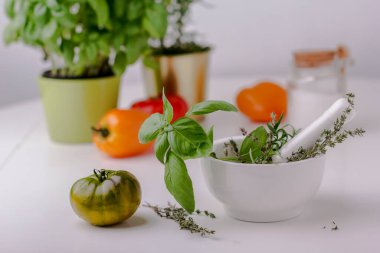 Beyaz seramik havan ve yeşil domatesli yeşil fesleğen. Alternatif bitkisel tıp konsepti. Yatay fotoğraf, beyaz üzerine izole edilmiş, metin için boşluk kopyala. Seçici odak.