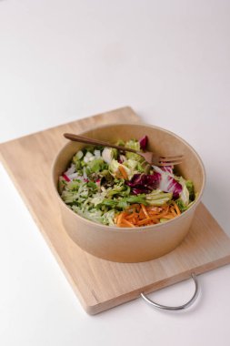 Kraft kağıdında beyaz bir masada çatallı sağlıklı bir salata. Şeritler halinde kesilmiş sebzeler ve otlar. Spor yemeği. - Öğle yemeği. Beslenme konsepti. Seçici odaklanma. Boşluğu kopyala.