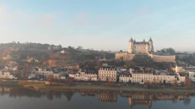Saumur kasabası, ortaçağ şatosu ve kilisesiyle gündoğumunda nehre yansıyan, Loire Vadisi, Fransa. Hava aracı görüntüsü, sağa dönüyor ve şehir ile nehri açığa çıkarıyor.