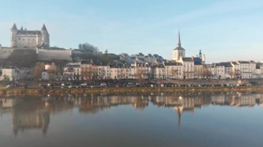 Saumur kasabası, ortaçağ şatosu ve kilisesiyle gündoğumunda nehre yansıyan, Loire Vadisi, Fransa. Hava aracı görüntüsü, sağa dönüyor ve şehir ile nehri açığa çıkarıyor.
